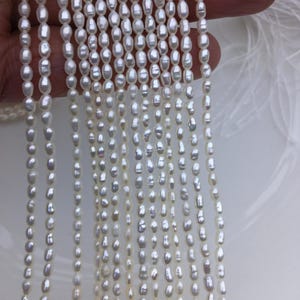 May include: A strand of white freshwater pearls, each pearl is oval shaped and has a slight irregular shape. The pearls are strung on a thin white thread.