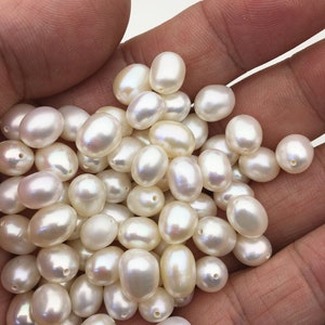 May include: A pile of white oval-shaped pearls in a hand. The pearls are smooth and lustrous.