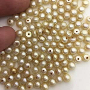 以下が含まれることがあります： わずかに金色がかったオフホワイトの丸い真珠が大量に積み重ねられています。真珠は滑らかで、わずかに虹色の光沢があります。