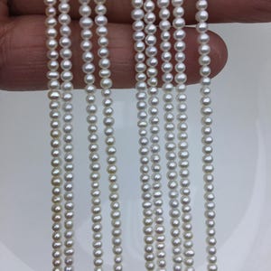 May include: A strand of white freshwater pearls, with multiple strands of pearls arranged side by side. The pearls are round and smooth, and they are strung on a clear thread.