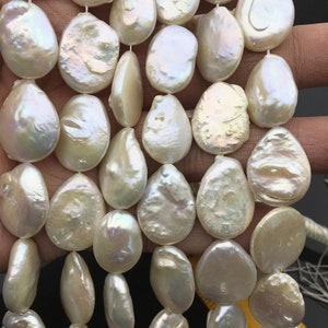 May include: Strand of lustrous, off-white baroque pearls. Each pearl has a unique, irregular shape and a shimmering surface. The pearls are strung together, ready for jewelry making. The pearls are approximately 1 inch in length.