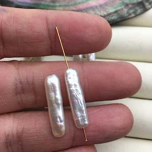 Puede incluir: Dos cuentas de perla barroca blanca con un alambre dorado enhebrado.