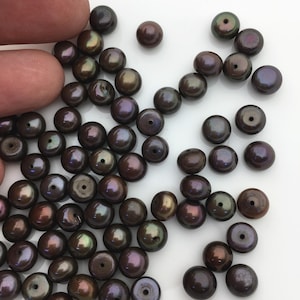 May include: A collection of dark brown and iridescent round pearls. The pearls have a smooth, glossy finish and are arranged in a loose pile.