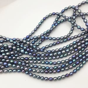 Può includere: Una lunga fila di piccole perle d'acqua dolce di forma ovale, caratterizzate da una palette di colori scuri e iridescenti con tonalità blu profondo, viola e grigio antracite. Le perle sono infilate in una linea continua e liscia.