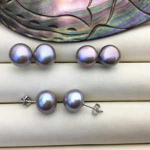 May include: A set of six pearl earrings. The earrings are a light purple colour and have a pearlescent sheen. The earrings are displayed on a white surface.