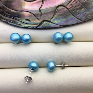 May include: A pair of blue pearl earrings with silver posts. The earrings are displayed on a white surface.