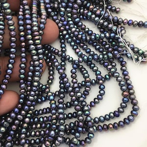 Peut inclure: Plusieurs brins de petites perles rondes aux reflets irisés bleu et violet foncé. Chaque perle présente un éclat métallique avec des nuances de vert et de bronze. Les perles sont enfilées sur un fil blanc fin, formant des brins fluides.