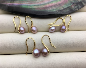 May include: A pair of gold dangle earrings with a single, light purple pearl on each earring.