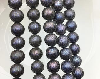 May include: Close-up of strands of dark grey, textured beads. The beads have a spherical shape with a patterned surface. The beads have a subtle iridescent sheen, reflecting hints of purple and blue. The background is a plain white surface.