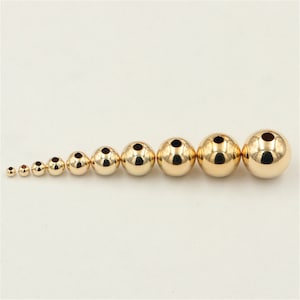 May include: A set of 10 gold-coloured metal beads of varying sizes. The beads are round and have a hole in the centre.