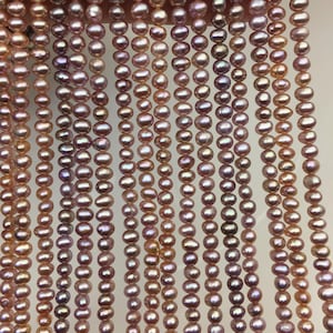 May include: Multiple strands of oval pearls in shades of pink, lavender, and peach. The pearls are strung together, creating a cascading effect. The pearls have a smooth, iridescent surface, reflecting light.