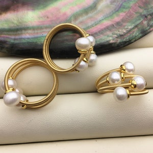 Könnte beinhalten: Zwei goldene Drahtringe mit weißen Perlen. Die Ringe sind gewickelt und haben mehrere Perlen angebracht.