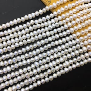 Puede incluir: Una hebra de perlas de agua dulce blancas, cada perla tiene una forma ligeramente irregular. Las perlas están enhebradas en un hilo blanco y tienen un tamaño aproximado de 6-7 mm.