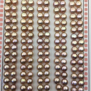 May include: A display of lustrous, peach-coloured pearls arranged in neat rows. The pearls have a subtle iridescence, reflecting light with hints of gold and pink. The card reads "High Fashion" in elegant script, suggesting a focus on jewellery or accessories.