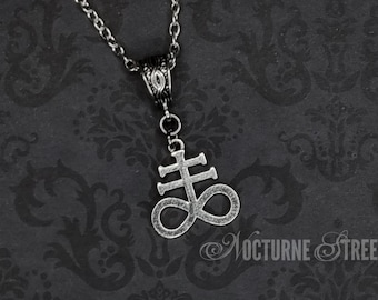 May include: A silver necklace with a pendant featuring the symbol of the Leviathan, a cross with a circle around it, on a black background.