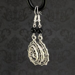 May include: Silver spider web earrings with black beads. The spider web design features a spider in the center.