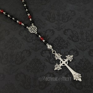 May include: A black and red beaded rosary necklace with a silver ornate cross pendant.