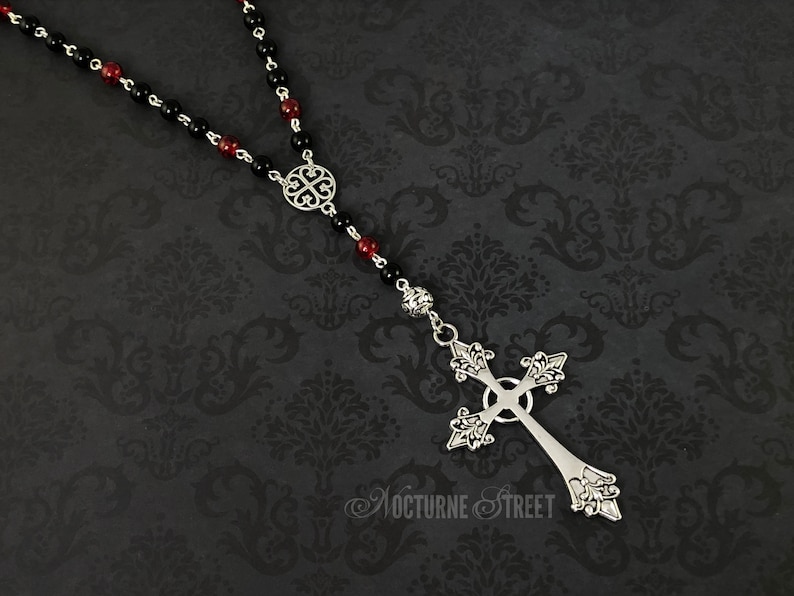 May include: A black and red beaded rosary necklace with a silver ornate cross pendant.