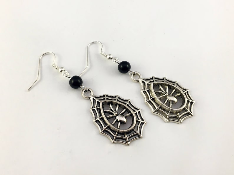 May include: A pair of silver spiderweb earrings with black beads. Each earring features a detailed spiderweb design with a small spider in the center.