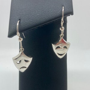 Op de afbeelding: Een paar zilveren oorhangers met een ontwerp van een vrolijk en verdrietig gezichtsmasker.