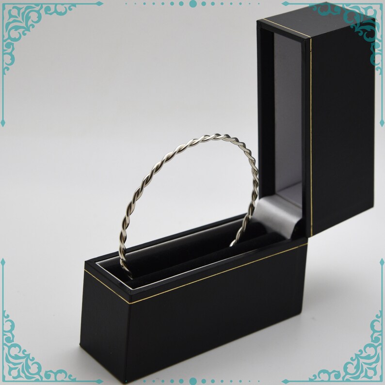 May include: A silver twisted bangle bracelet in a black velvet lined jewelry box with a gold trim.