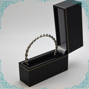 May include: A silver twisted bangle bracelet in a black velvet jewelry box with a gold trim.