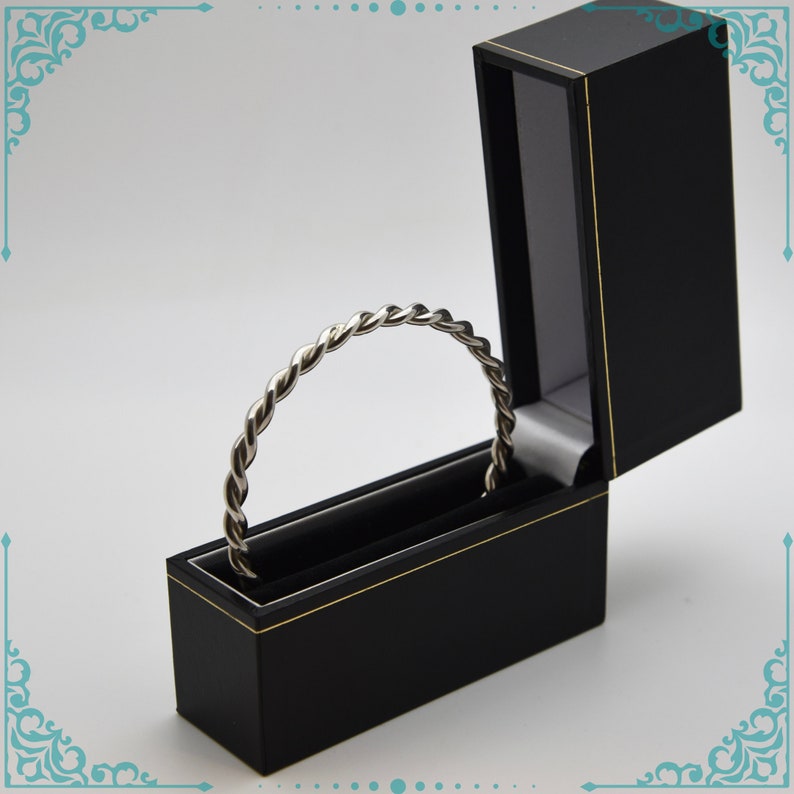 May include: A silver twisted bangle bracelet in a black velvet jewelry box with a gold trim.