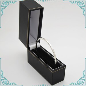 May include: A silver bangle bracelet in a black velvet lined box with a gold trim.