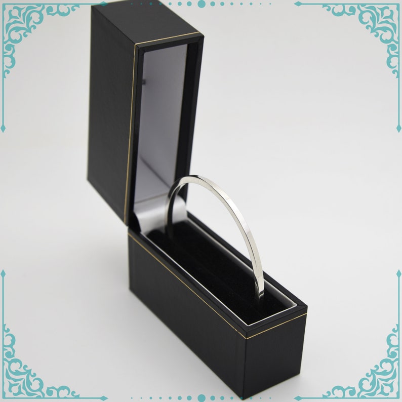 May include: A silver bangle bracelet in a black velvet lined box with a gold trim.