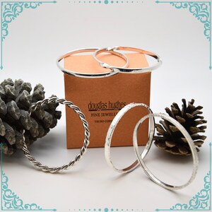May include: Four silver bangles, one with a twisted rope design, on a brown box with the text "douglas hughes fine jewellery truro cornwall".