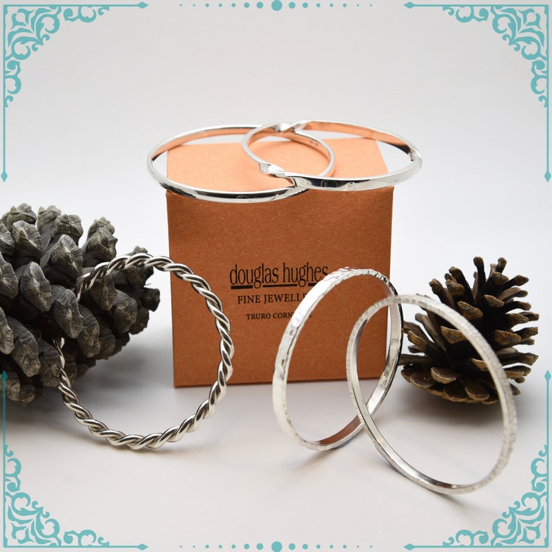 May include: Four silver bangles, one with a twisted rope design, on a brown box with the text "douglas hughes fine jewellery truro cornwall".