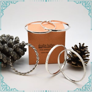 May include: Four silver bangles, one with a twisted design, on a brown box with the text "douglas hughes fine jewellery truro cornwall".