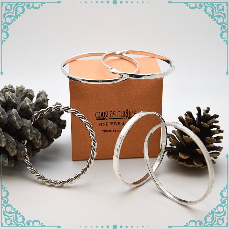May include: Four silver bangles, one with a twisted design, on a brown box with the text "douglas hughes fine jewellery truro cornwall".