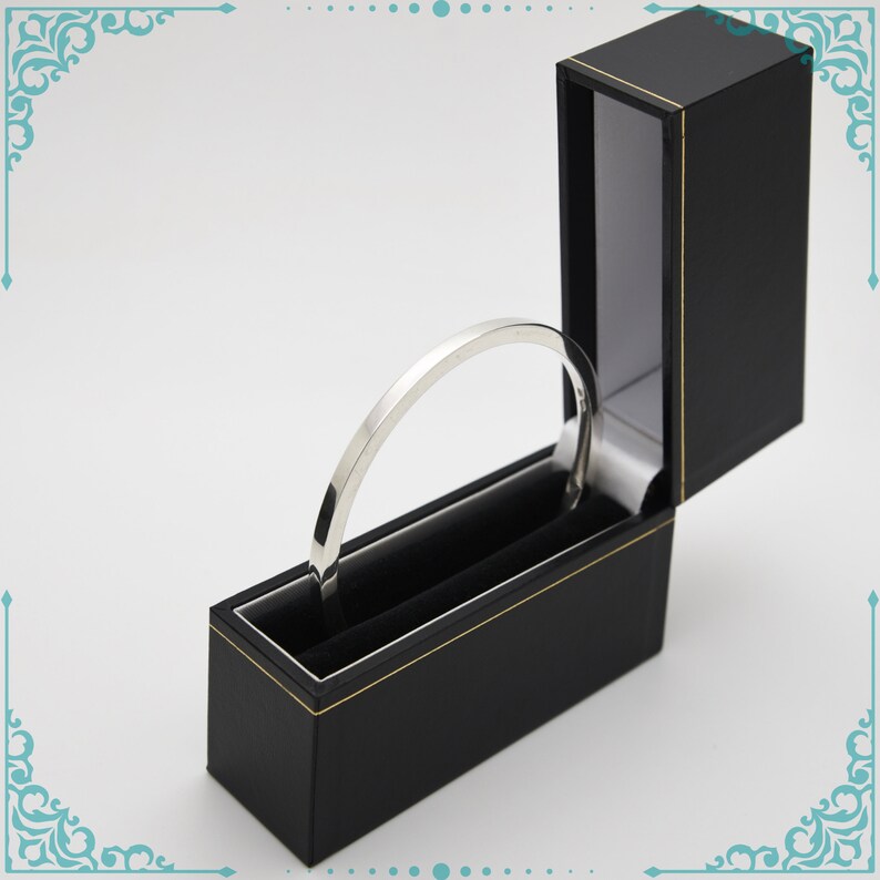 May include: A silver bangle bracelet in a black velvet lined box with a gold trim.