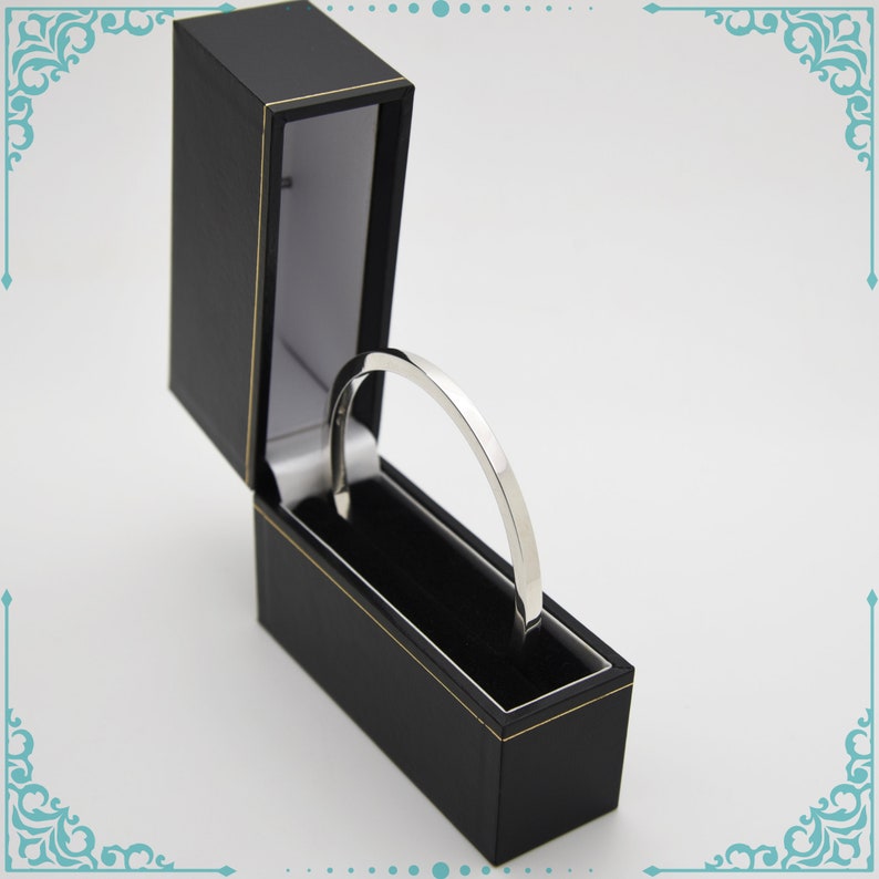 May include: A silver bangle bracelet in a black velvet jewelry box with a gold trim.