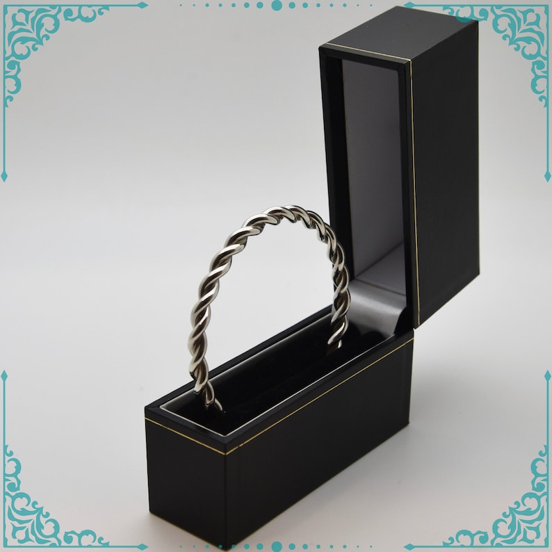 May include: A silver twisted bangle bracelet in a black velvet jewelry box with a gold trim.