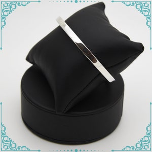 May include: A silver bangle bracelet on a black display stand.