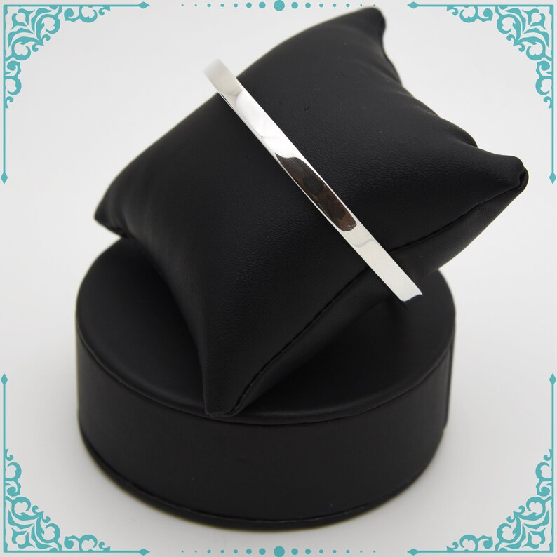 May include: A silver bangle bracelet on a black display stand.