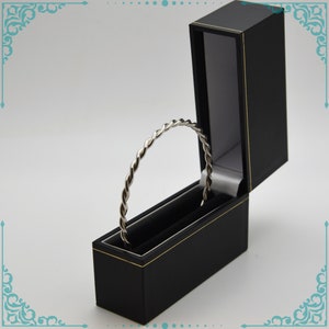 May include: A silver twisted bangle bracelet in a black velvet lined box with a gold trim.