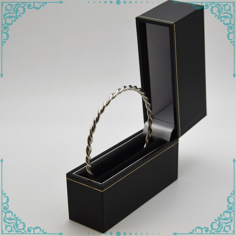 May include: A silver twisted bangle bracelet in a black velvet lined box with a gold trim.