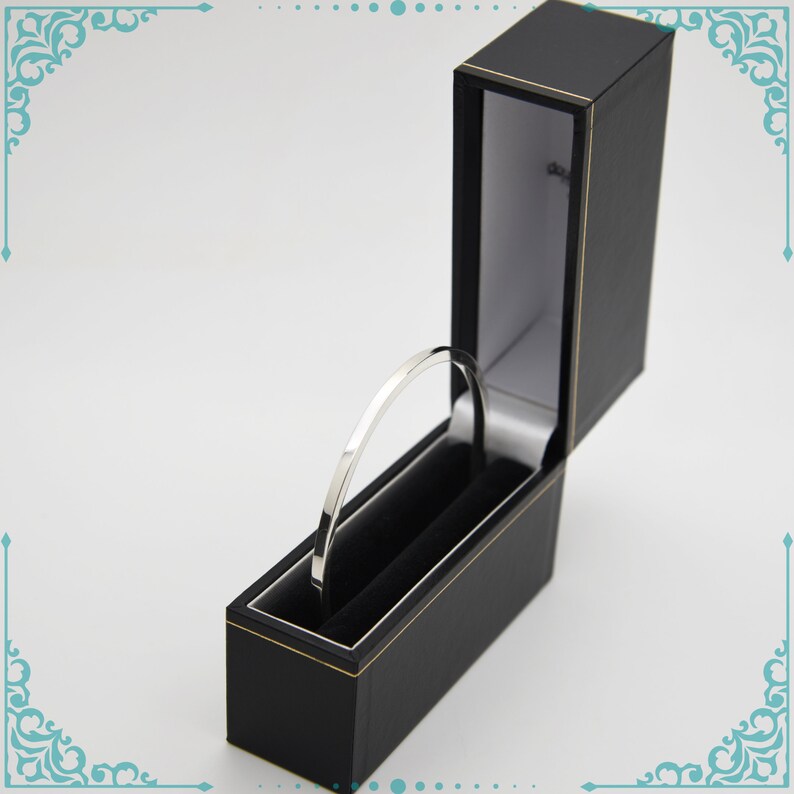 May include: A silver bangle bracelet in a black velvet lined box. The box is open and the bracelet is sitting inside.