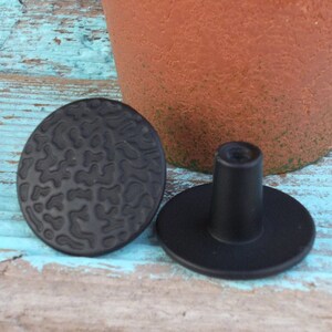 May include: Two black cabinet knobs with a textured, abstract design. One knob is round and the other is round with a raised post.