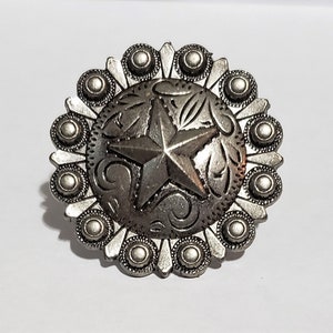May include: Silver-toned metal concho with a five-pointed star design and floral accents. The concho has a circular shape with a scalloped edge.