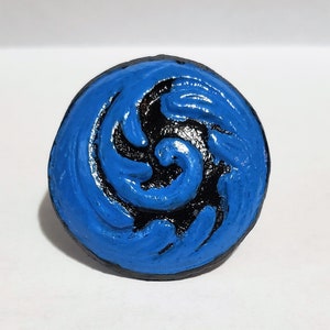 May include: A round, blue and black ceramic knob with a swirling design. The knob has a raised, textured design.