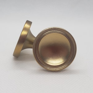 May include: Two gold-toned metal cabinet knobs with a round, slightly domed top and a short, cylindrical base.
