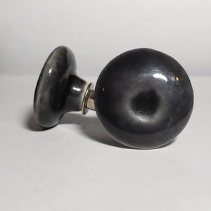 May include: Two black ceramic door knobs with a shiny finish. The knobs have a round shape with a slight indentation in the center.