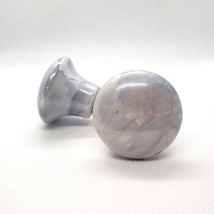 May include: A white and gray ceramic door knob with a swirl pattern. The knob has a round shape and a small, flat base.