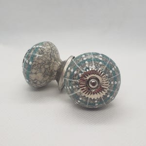 May include: Two decorative ceramic cabinet knobs. One knob is teal with white polka dots and a silver metal base. The other knob is a speckled gray and white pattern. The knobs are for furniture hardware.