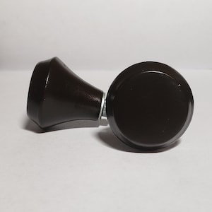 May include: A dark brown wooden finial with a round top and a smaller, cone-shaped base. The finial is designed for use with curtains or drapes.