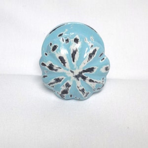 May include: A light blue cabinet knob with a white and black distressed paint design.